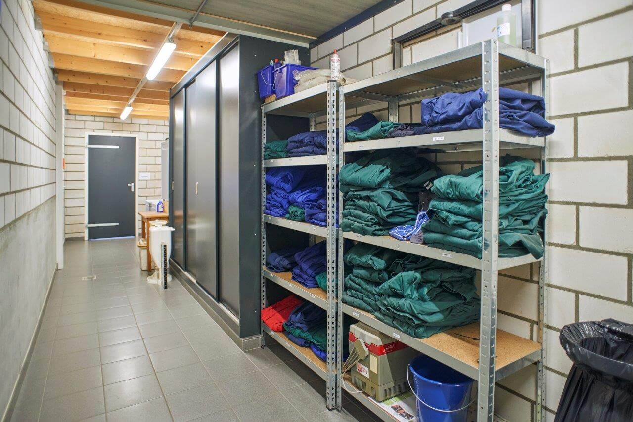 Op een ruime gang de omkleedruimte en de douches is een nette opslagruimte gemaakt. Achterin is de deur naar de bedrijfskantine. Daar komt niemand zonder eerst door de hygiënesluis te zijn gegaan. Wel is die ruimte uitgerust met ramen om zicht te hebben op de ingang van de stal.